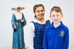 Students at St Catherine Laboure Catholic Primary School Gymea smiling in front of statue of St Agnes